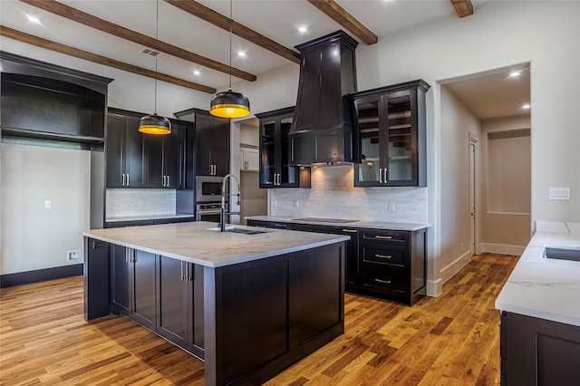 kitchen with light stone countertops, a kitchen island with sink, hardwood / wood-style floors, decorative light fixtures, and decorative backsplash