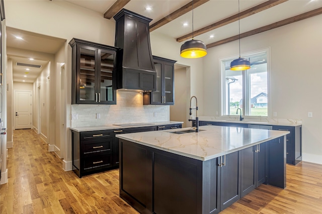 kitchen with a kitchen island with sink, sink, hanging light fixtures, light hardwood / wood-style floors, and light stone counters