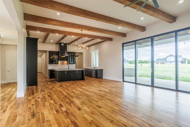 unfurnished living room with beamed ceiling, ceiling fan with notable chandelier, sink, and light hardwood / wood-style flooring