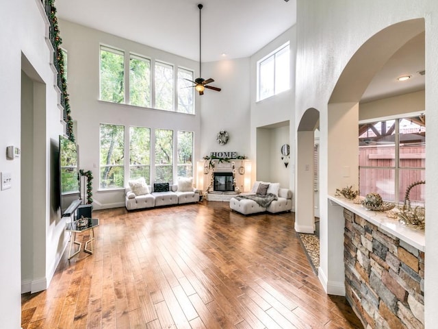 living room with hardwood / wood-style flooring, a fireplace, ceiling fan, and a high ceiling