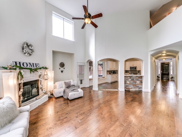 living room with hardwood / wood-style flooring, ceiling fan, a fireplace, and a high ceiling