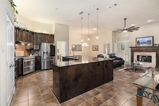 kitchen featuring appliances with stainless steel finishes, ceiling fan, hanging light fixtures, dark brown cabinets, and a stone fireplace