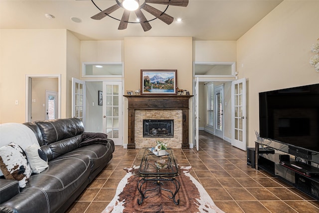 living room with ceiling fan, french doors, a stone fireplace, and dark tile patterned floors