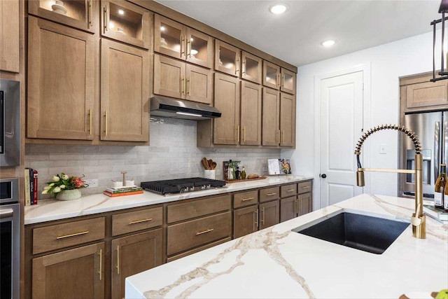 kitchen featuring decorative light fixtures, sink, decorative backsplash, light stone counters, and stainless steel appliances