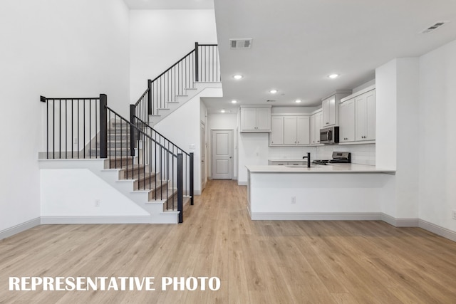 kitchen featuring appliances with stainless steel finishes, white cabinets, light hardwood / wood-style floors, and kitchen peninsula