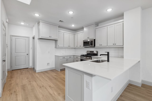 kitchen with tasteful backsplash, sink, kitchen peninsula, stainless steel appliances, and light hardwood / wood-style flooring