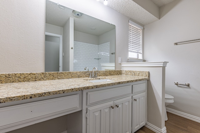 bathroom with a textured ceiling, vanity, tiled shower, hardwood / wood-style floors, and toilet