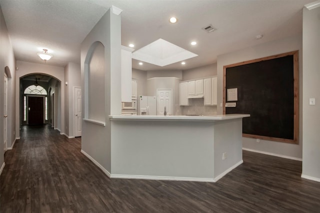 kitchen featuring kitchen peninsula, a skylight, dark wood-type flooring, white refrigerator with ice dispenser, and white cabinetry