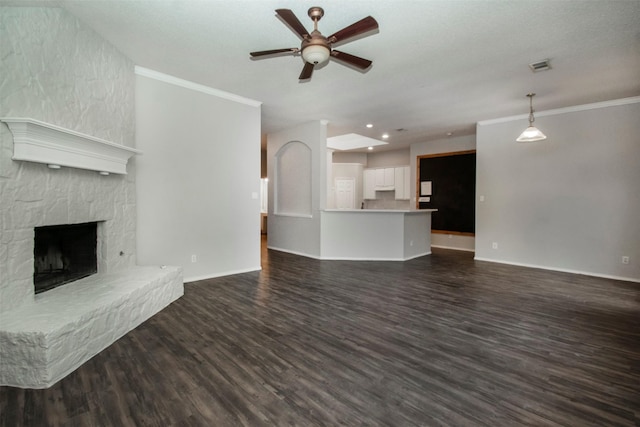 unfurnished living room with a stone fireplace, crown molding, dark hardwood / wood-style floors, ceiling fan, and a textured ceiling