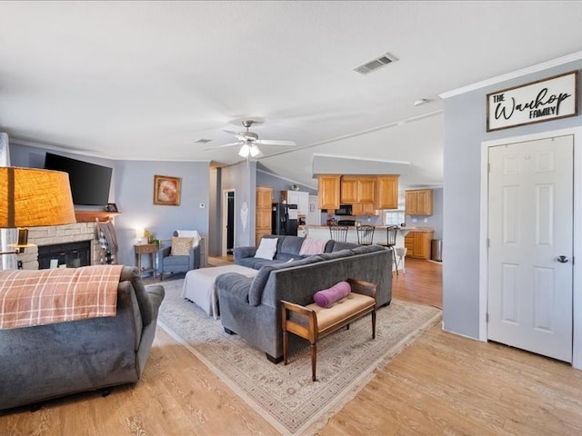 living room with a stone fireplace, ceiling fan, light hardwood / wood-style floors, and ornamental molding