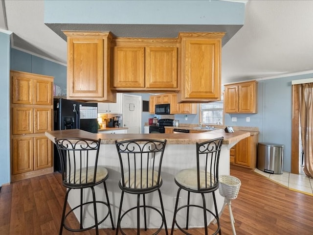 kitchen with hardwood / wood-style floors, a kitchen island, crown molding, and black appliances