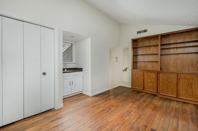 unfurnished bedroom with sink, light hardwood / wood-style floors, a closet, and vaulted ceiling