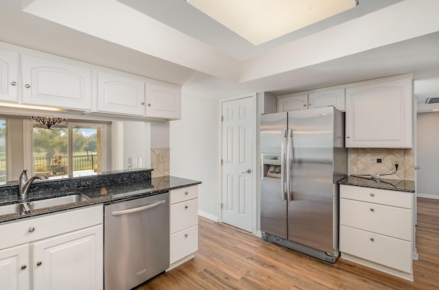 kitchen with stainless steel appliances, white cabinetry, dark stone countertops, and tasteful backsplash