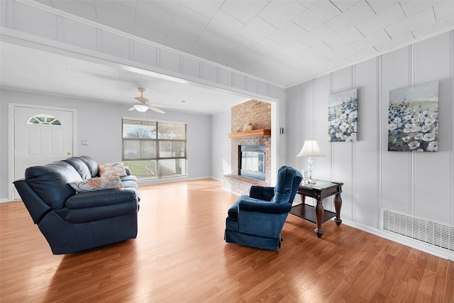 living room featuring a fireplace, wood-type flooring, ceiling fan, and crown molding