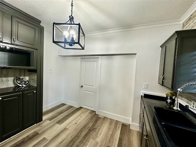 kitchen with dark brown cabinetry, crown molding, sink, light hardwood / wood-style flooring, and a chandelier