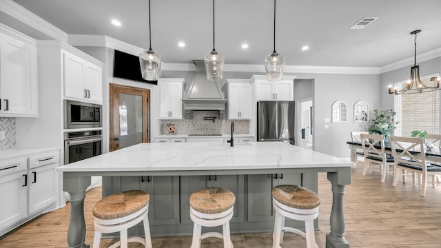 kitchen featuring a center island with sink, decorative light fixtures, light stone counters, and appliances with stainless steel finishes