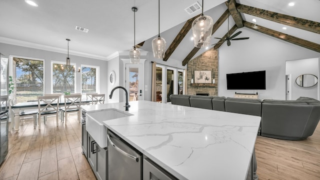 kitchen featuring lofted ceiling with beams, decorative light fixtures, stainless steel dishwasher, and an island with sink