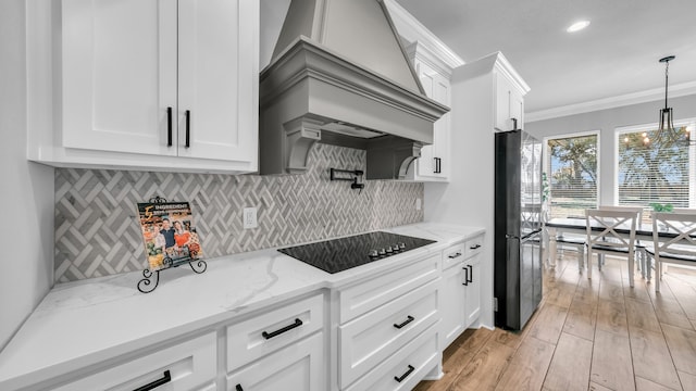 kitchen featuring premium range hood, black appliances, white cabinets, crown molding, and hanging light fixtures