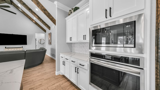 kitchen with light stone countertops, stainless steel appliances, vaulted ceiling with beams, light hardwood / wood-style floors, and white cabinets