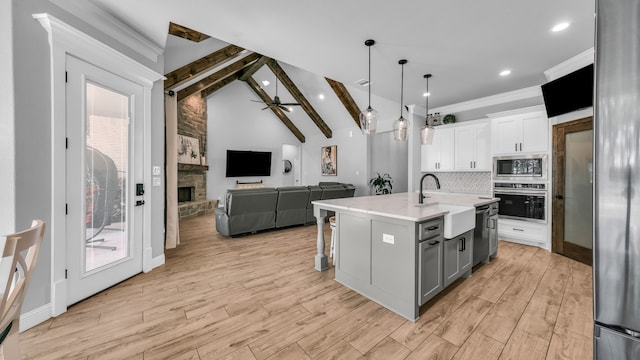 kitchen featuring sink, stainless steel appliances, lofted ceiling with beams, an island with sink, and white cabinets