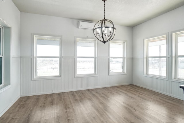 unfurnished dining area with a wall mounted air conditioner, light wood-type flooring, a wealth of natural light, and a notable chandelier