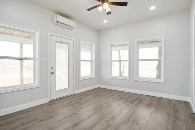 interior space featuring a wall mounted air conditioner, ceiling fan, a wealth of natural light, and light hardwood / wood-style flooring