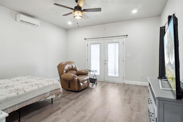 bedroom with a wall mounted AC, ceiling fan, french doors, and light wood-type flooring