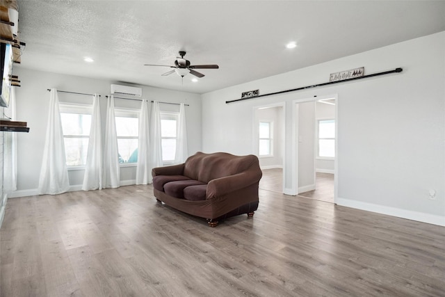 living room with a wealth of natural light, light hardwood / wood-style flooring, a wall mounted AC, and ceiling fan