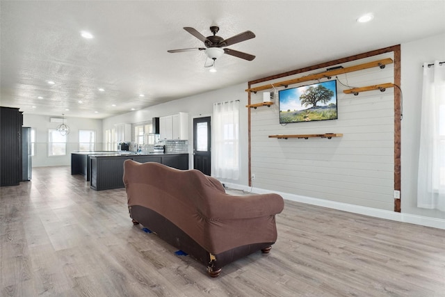 living room featuring ceiling fan, light wood-type flooring, and wooden walls