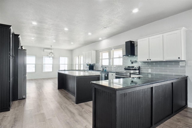 kitchen with a center island, wall chimney exhaust hood, appliances with stainless steel finishes, white cabinetry, and kitchen peninsula