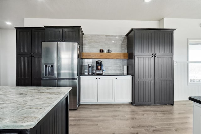 kitchen with stainless steel fridge with ice dispenser, light hardwood / wood-style floors, light stone counters, and white cabinetry