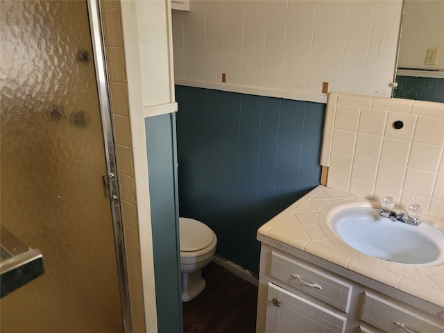 bathroom with vanity, toilet, a shower with door, and wooden walls