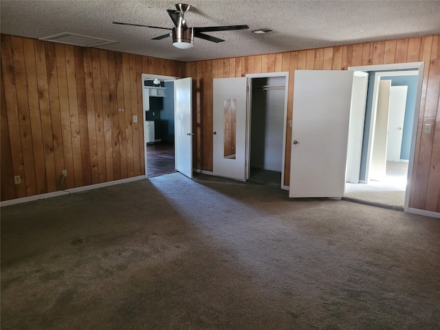 unfurnished bedroom with ceiling fan, wood walls, a textured ceiling, and dark carpet