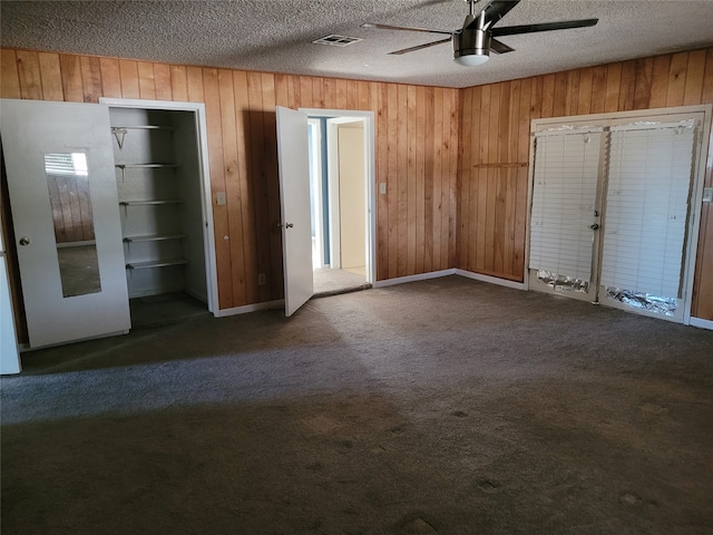 unfurnished bedroom featuring carpet, a textured ceiling, ceiling fan, and wood walls