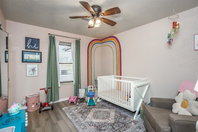 bedroom with wood-type flooring, a nursery area, and ceiling fan