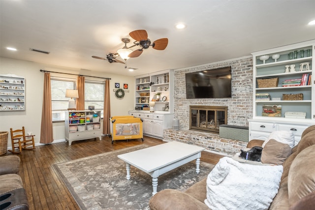 living room featuring built in shelves, ceiling fan, dark hardwood / wood-style floors, and a brick fireplace