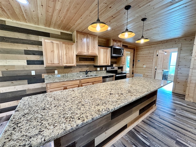 kitchen with appliances with stainless steel finishes, light stone counters, wooden walls, light brown cabinets, and pendant lighting