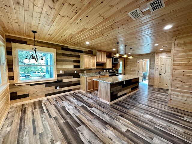 kitchen with wood walls, light stone countertops, hanging light fixtures, and dark wood-type flooring