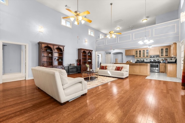 living room featuring ceiling fan with notable chandelier, wood-type flooring, and a towering ceiling