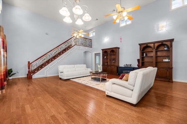 living room with a high ceiling, ceiling fan with notable chandelier, and light wood-type flooring