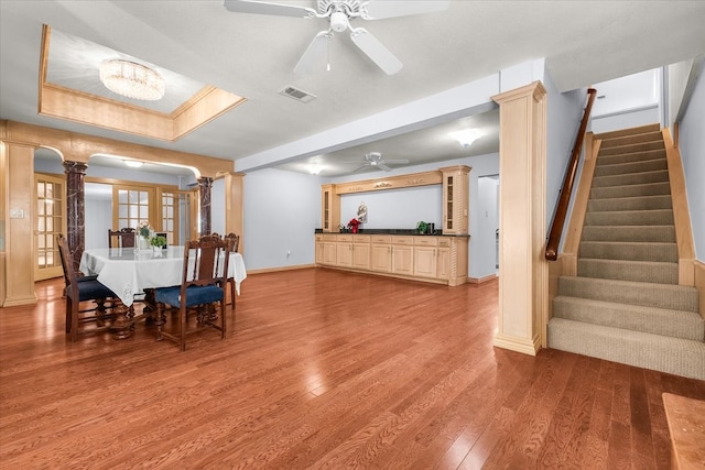 dining area featuring ceiling fan with notable chandelier, a raised ceiling, ornate columns, and light hardwood / wood-style flooring