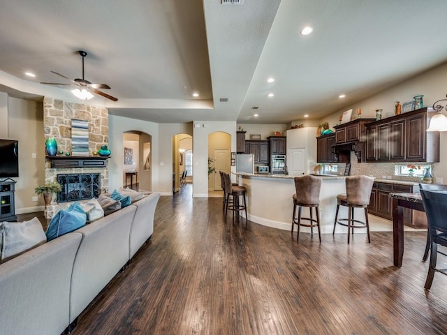 living room featuring a tray ceiling, a stone fireplace, dark hardwood / wood-style floors, and ceiling fan