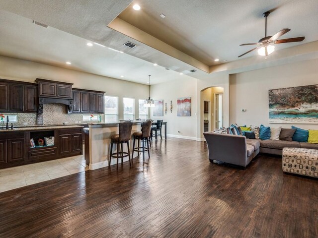 kitchen with appliances with stainless steel finishes, tasteful backsplash, a kitchen island with sink, light stone countertops, and dark brown cabinets