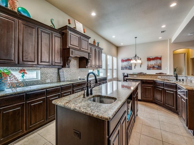 kitchen featuring dark brown cabinetry, sink, decorative light fixtures, a center island with sink, and dishwasher