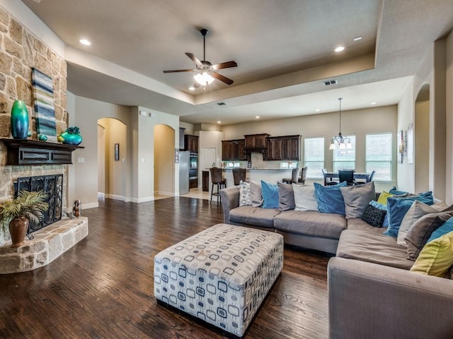 living area featuring a tray ceiling, a stone fireplace, dark wood finished floors, and arched walkways