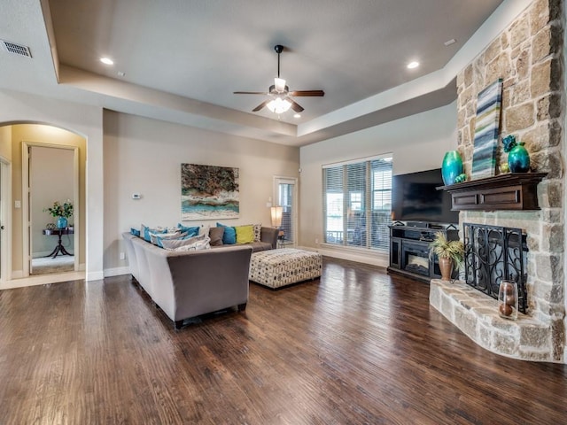 living room with dark wood-style floors, visible vents, a raised ceiling, and a stone fireplace