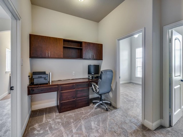 home office with light colored carpet, a towering ceiling, and baseboards