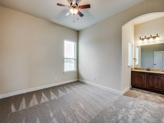 empty room featuring light carpet, baseboards, arched walkways, and ceiling fan