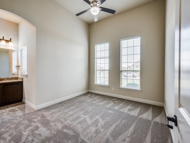 unfurnished room featuring arched walkways, light carpet, ceiling fan, and baseboards