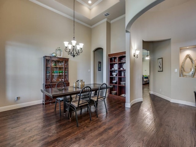 dining room with dark hardwood / wood-style flooring, a high ceiling, a notable chandelier, a raised ceiling, and crown molding